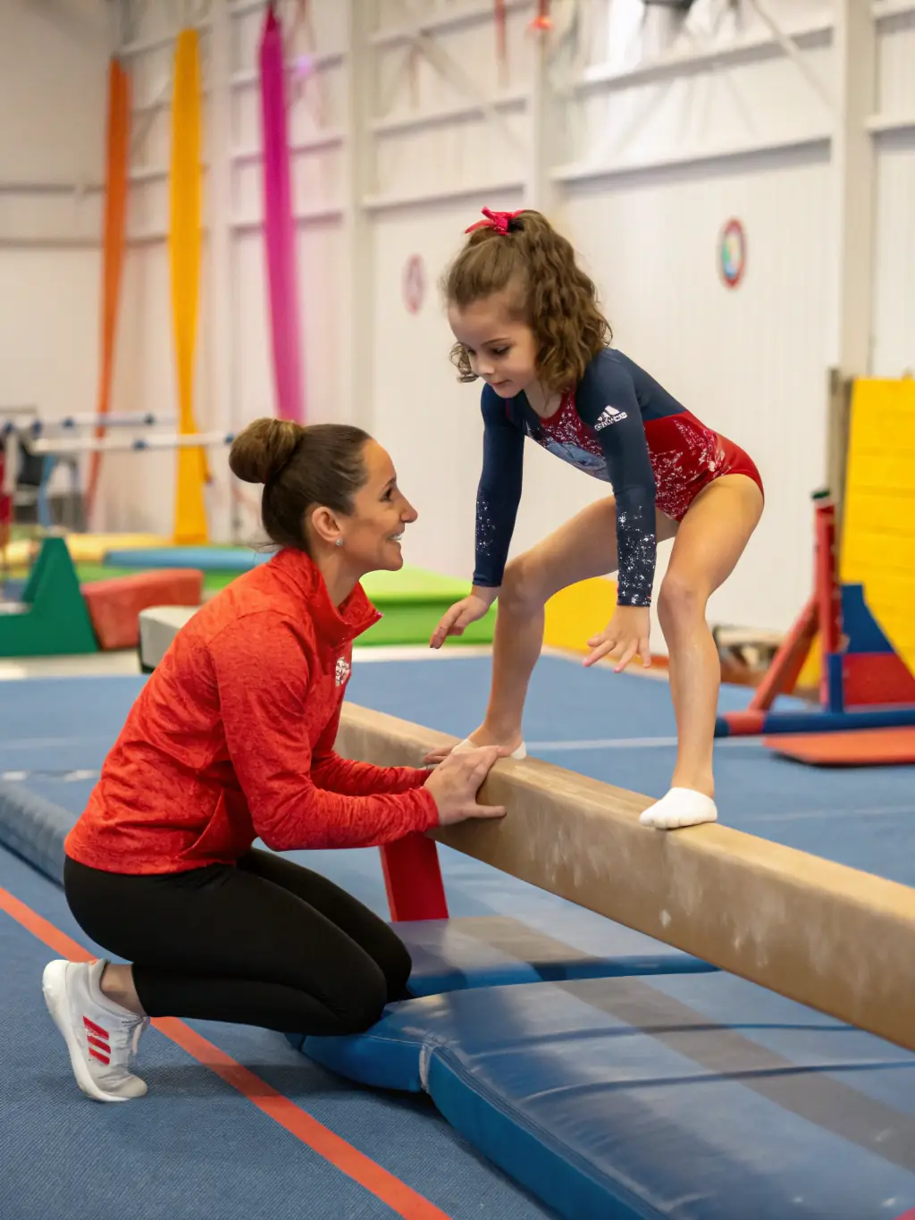 A group of young children participating in a gymnastics class at D.U.C., focusing on balance and coordination exercises, with a coach guiding them.